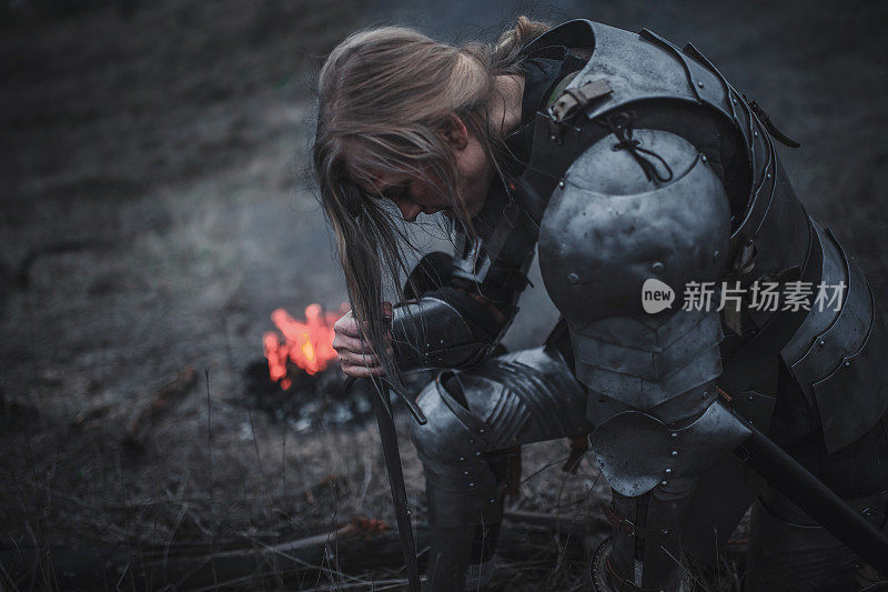 在Jeanne d'Arc的形象中，女孩跪在火和烟的背景下，身穿盔甲，手握宝剑。